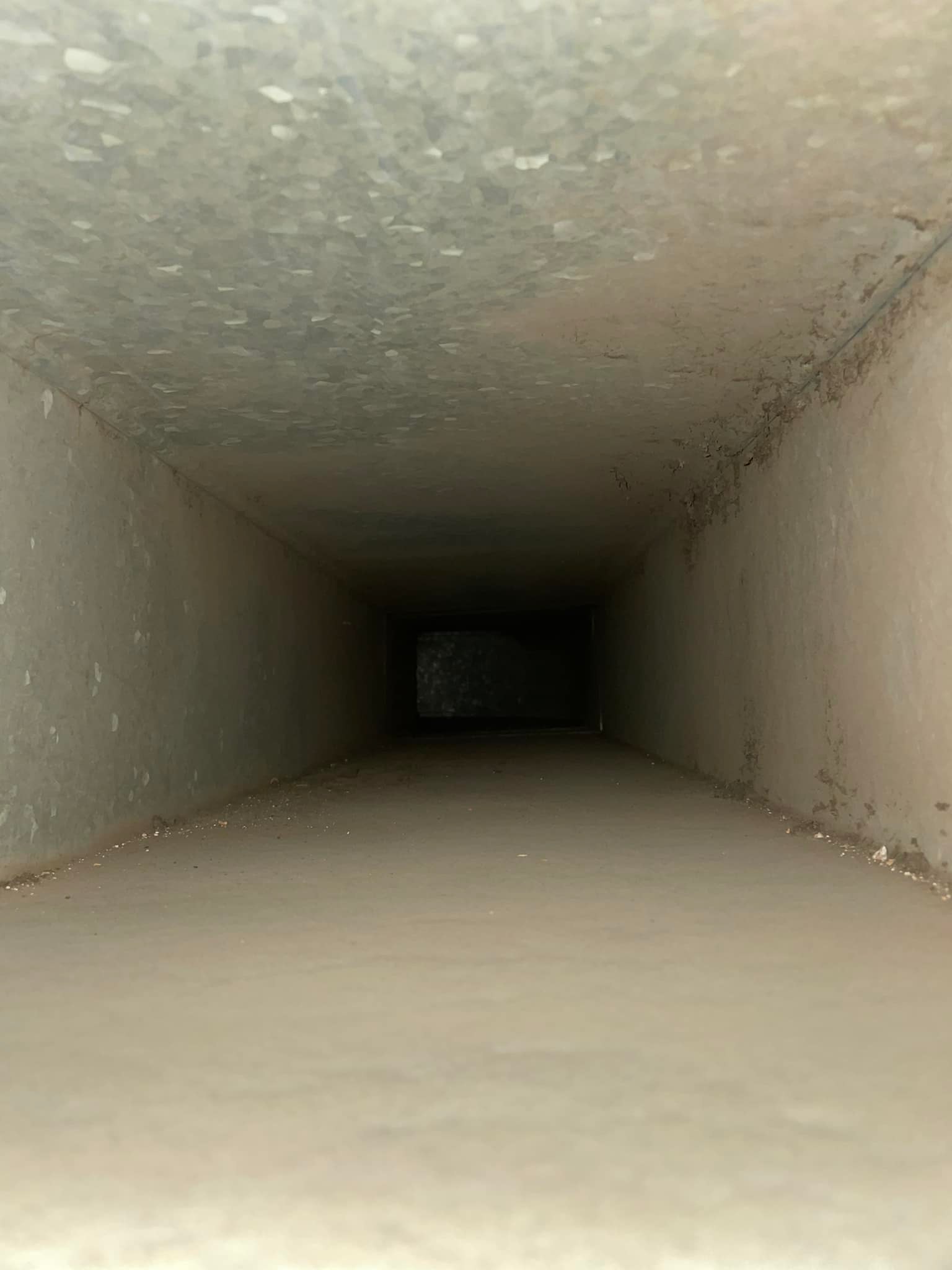 Inside view of an empty, rectangular air duct with visible dust on the surface.