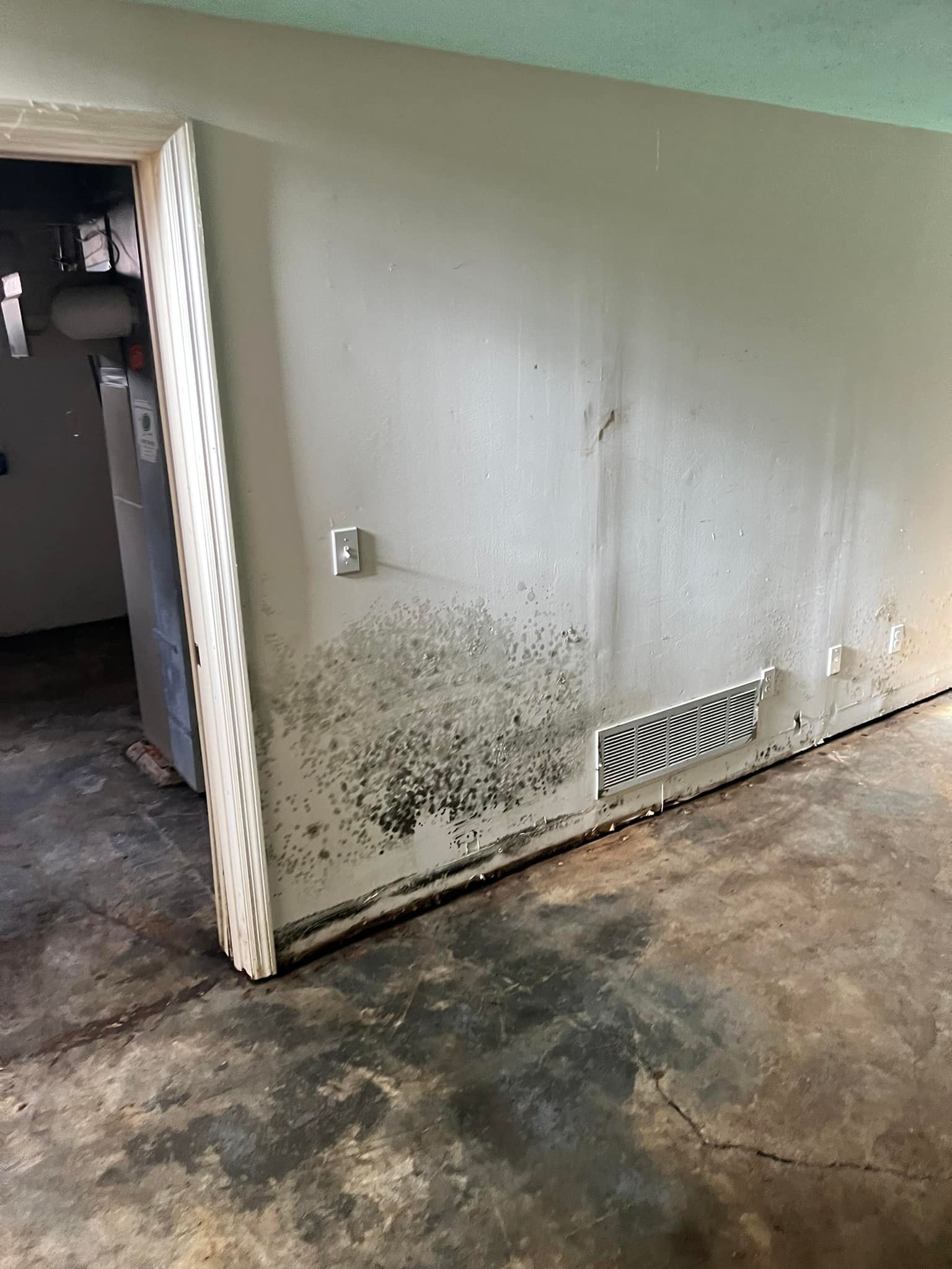 Wall with visible black mold near a doorway, adjacent to an air vent, and stained concrete floor.
